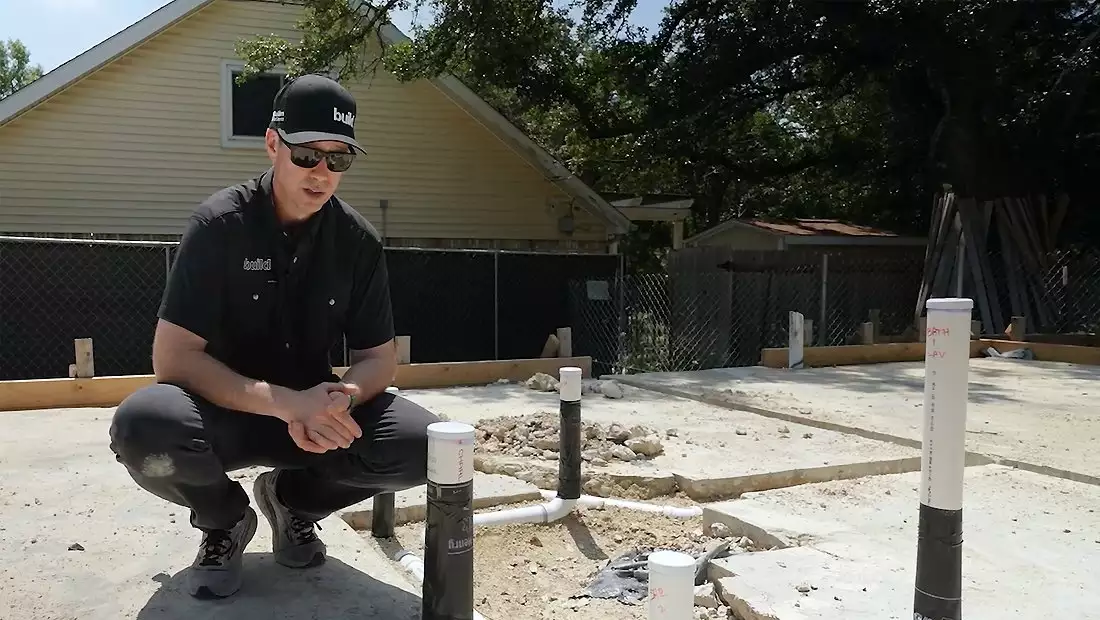 Matt Risinger Kneeling by Some PVC Pipes Coming Up from Austin Build Foundation
