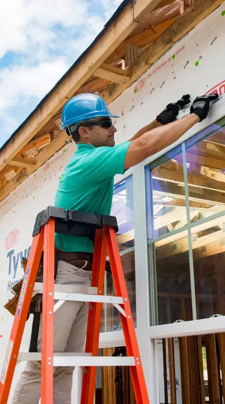 Worker Applying Housewrap to House Under Construction
